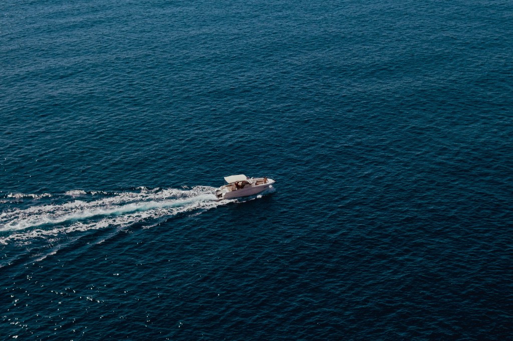 Small white boat cruising on deep blue water seen from above